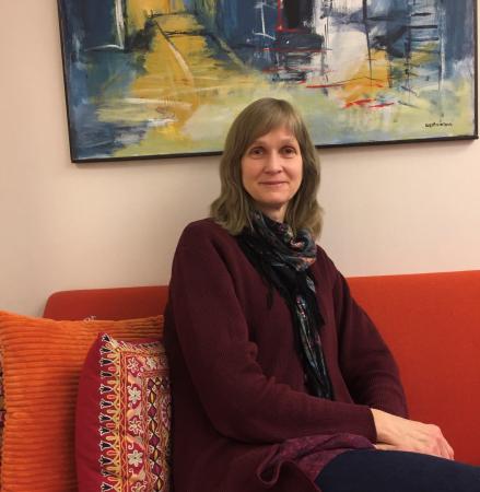 Ulrika har ljusbrunt, halvlångt hår och är iklädd en vinrödtröja, svart mönstrad sjal och svarta jeans. Hon sitter i Taltidningens knalloranga soffa framför en oljemålning i blå, gula och vita nyanser