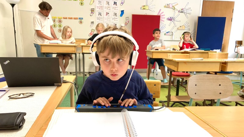 Walter sitter i klassrummet med hörlurar på. Han skriver på sin punktdisplay  och ser koncentrerad ut. Han har mellanblont hår och bär en blårandig tröja.