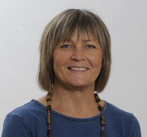 Catharina Månsson har en kort frisyr och mörkt hår. Hon bär en blå tröja på bilden och ett flerfärgat halsband. Hon ser glad ut.