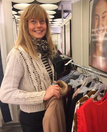 Ann-Sofie Sköld Åberg klädd i naturvit kofta och svart-vit randig sjal håller i en sandbrun kappa med fuskpälskrage. Hon har på en klädstång hängt olika reafynd. Längst fram en signalröd klänning med volanger.