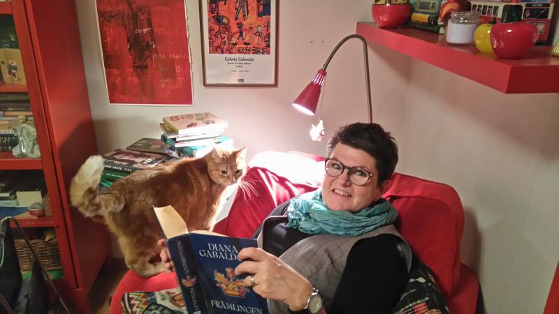 Agneta sitter i sin röda läsfåtölj med den brandgula katten Nemo bredvid sig. 