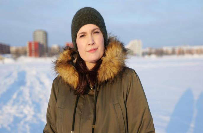 Carrie står på isen framför södra hamn i Luleå. Hon har en grå luva och militärgrön jacka med pälskrage. Hon ser bestämd ut!