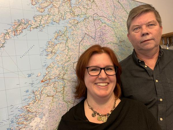 Petra och Roger står framför en karta över Norrbotten. Petra har rödbrunt hår och matchande glasögon. Roger har brungrått hår och säger att han aldrig ler på bild!
