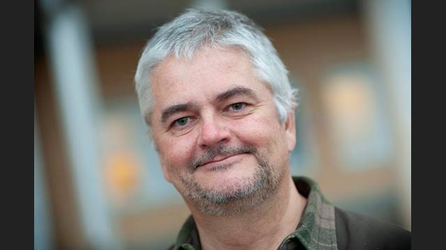 Anders har grått kort hår, ser glad ut och har en mossgrön skjorta.