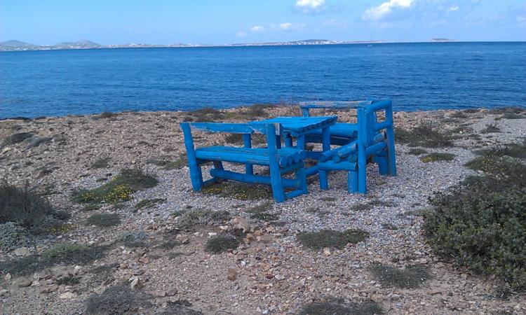 Blåmålade stolar och ett bord på en strand i Grekland.