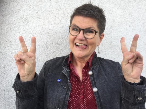 Agneta har kort, mörkt hår och glasögon med mörk båge. Hon ser glad ut.