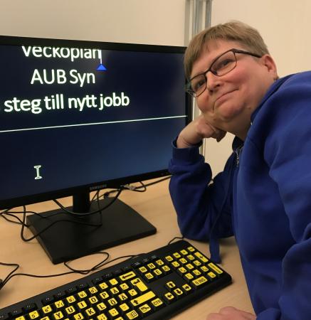 Jeanette Gustafsson har kortklippt brunt hår och glasögon. Hon har en blå kofta på sig och sitter framför en datorskärm där texten är förstorad.