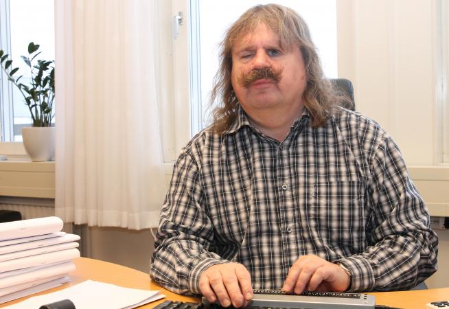 Håkan har grått långt hår och en stor mustasch.