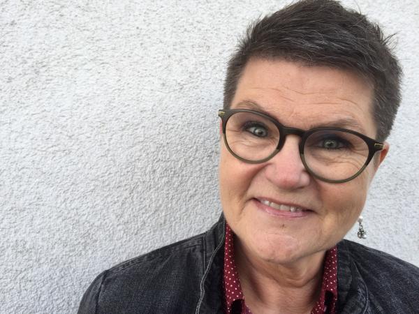 agneta har kort, mörkt hår och glasögon med mörk båge. Hon ser glad ut.