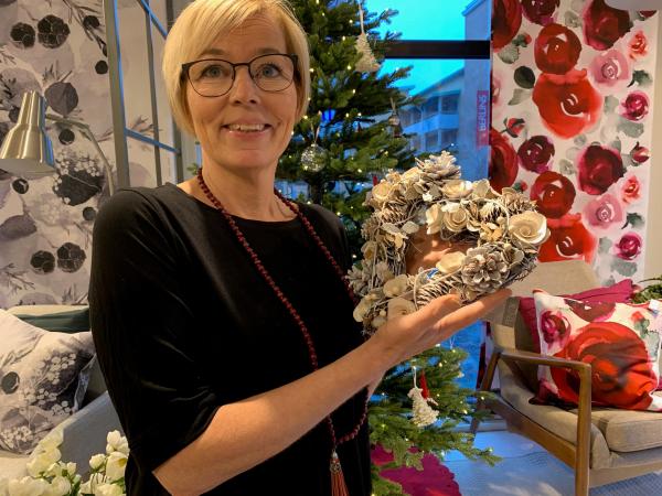 Annika Olsson har kort ljust hår och glasögon. Hon har en svart tröja och håller i en hjärtformad krans i vitt och silver.