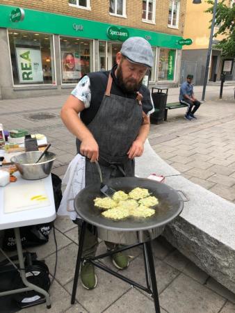 Pelle Johansson är klädd i förkläde och keps. Han steker grönsaksbiffar på en morikka vid ett stånd på Bondens egen marknad