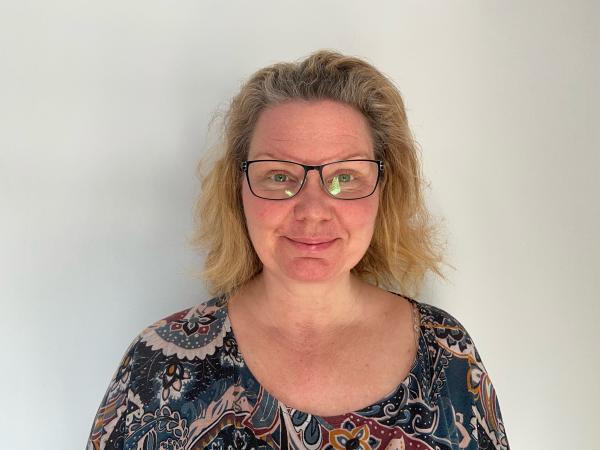 Johanna är blond med axellångt hår. Hon bär glasögon och ser glad ut i en mörkbrokig blus.