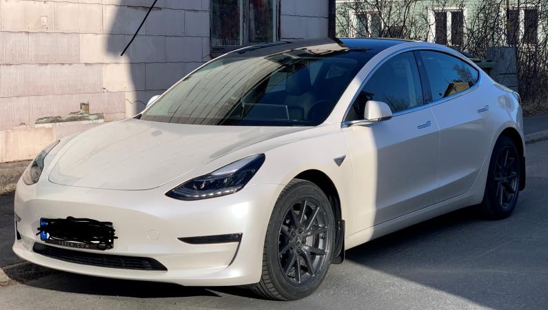Bilden föreställer en vit Tesla. En lyxig elbil som står parkerad framför ett hus.