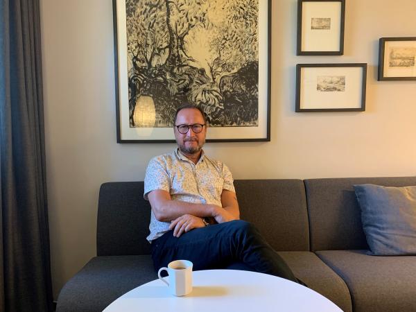 Roger har kort hår, bär glasögon och sitter i kommunikationsavdelningens fikahörna med en kopp kaffe framför sig.