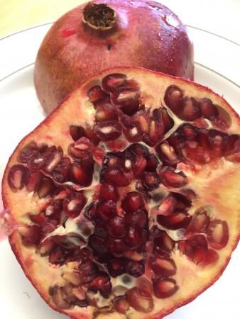Ett uppskuret granatäpple fyllt av röda glansiga kärnor vilar mot en hel frukt i bakgrunden