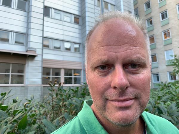 Lars Nyberg har kortklippt, grått hår. Han har en grön tröja och har ett silvergrått kontorshus i bakgrunden.