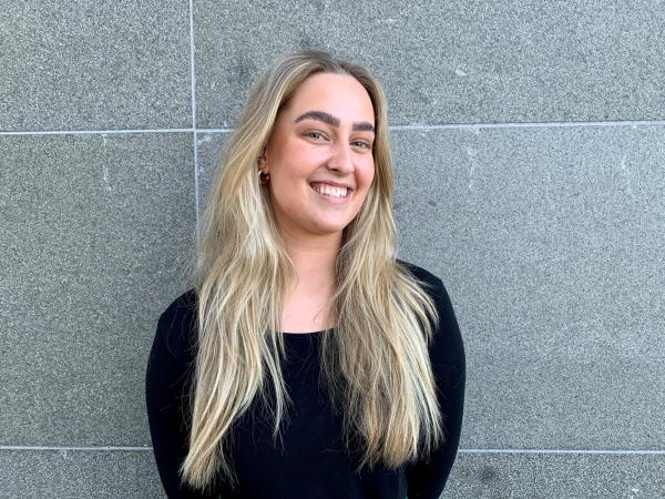 Rebecca har långt blont hår med mittbena och bär en svart tröja. Hon har svarta, burriga ögonbryn och ser helt osminkad ut. Hon ler på porträttbilden som är tagen framför en grå vägg med stenplattor