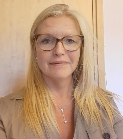 Siv Öhlund har långt, ljust hår  och glasögon med ljusbruna bågar. Hon har en beigefärgad skjorta på sig.