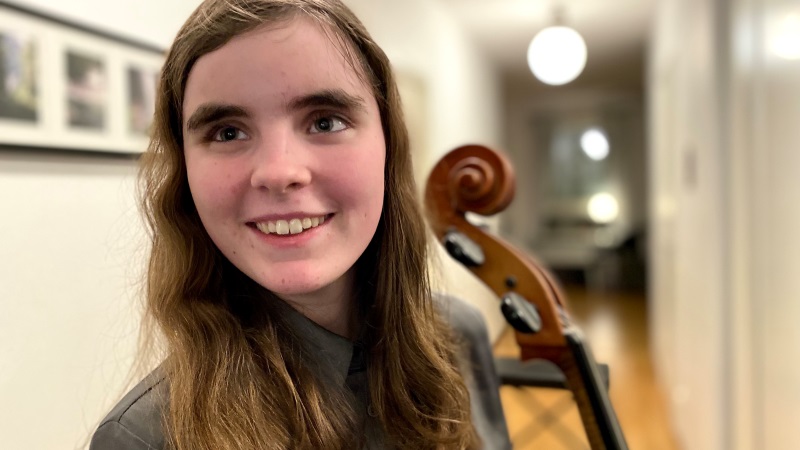 Liv har långt mellanbrunt hår och står med sin cello som man ser en bit av. Linn ser glad ut.