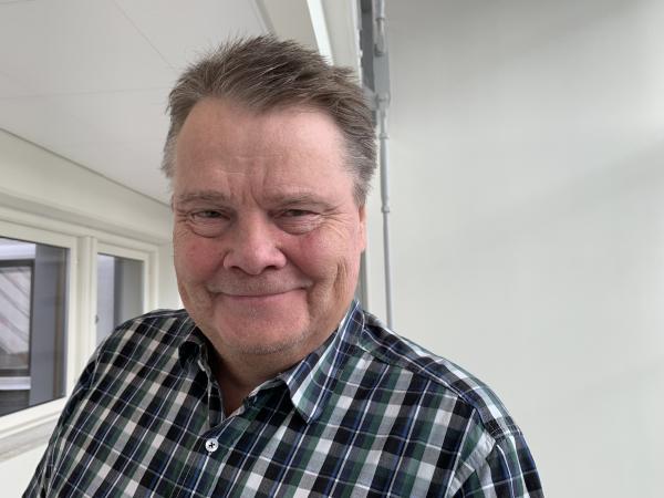 Ulf har kort hår och bär en gråvit rutig skjorta. Han ser glad ut.